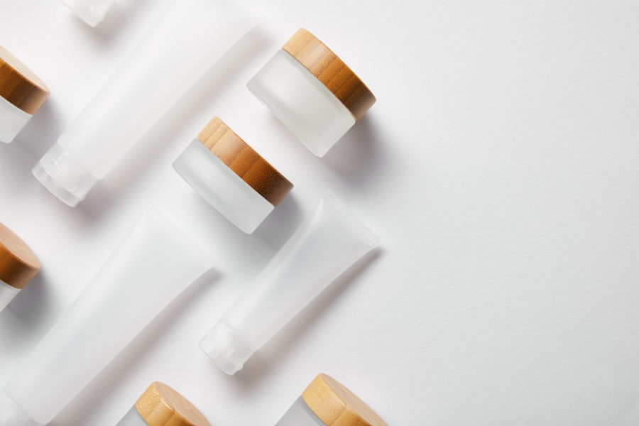 flat lay of cream tubes and jars with wooden caps on white